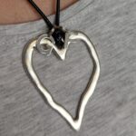 close-up of a silver-toned heart pendant with a silver G on one side and an F on the other
