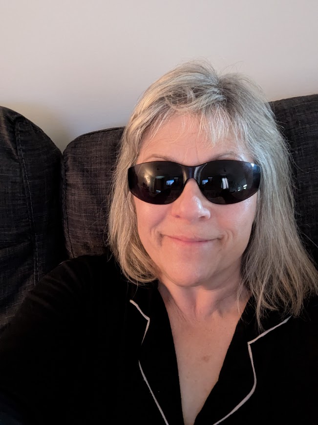 Smiling with unkempt hair, wraparound sunglasses, and wearing PJs.