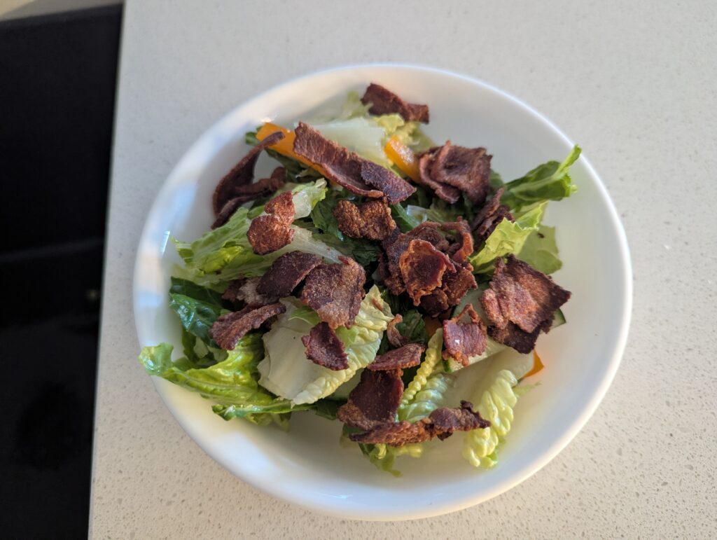 A small romaine salad with bits of bell peppers, cucumber, and a layer of crumbled, crispy bacon on top. 