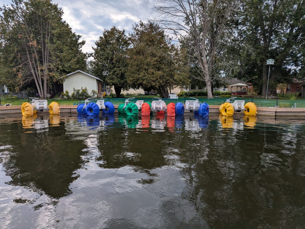 Five pedgal boats that look like tractors with massive back "tires" in either yello, blue, red, or green.