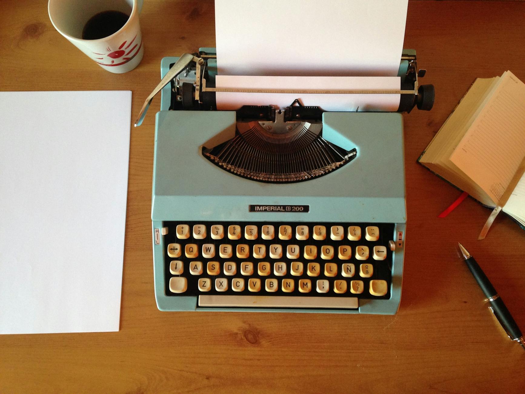 teal typewriter beside printer paper