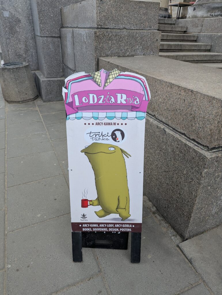 a sandwich board sign showing a cartoon character, a happy green monster, holding a cup of cofeee