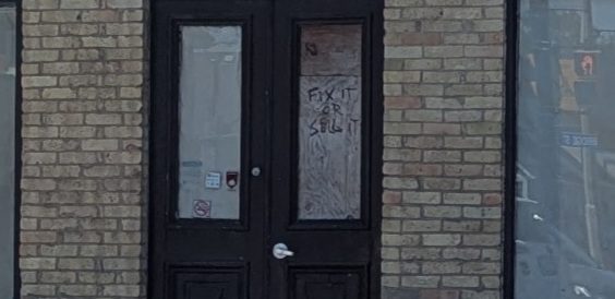 Close-up of a board over the door on a shuttered cafe where someone has scrawled, FIX IT OR SELL IT.