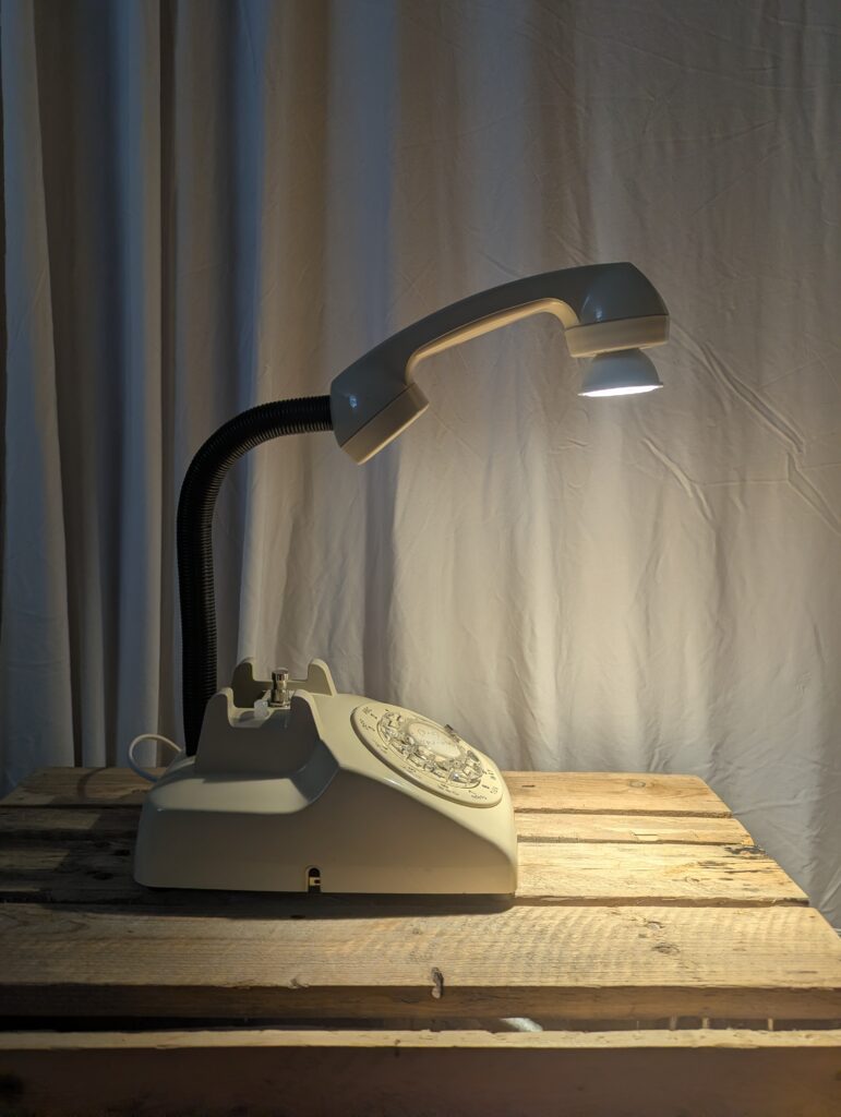 Beige rotaty phone with the reciever above the body, attached to a movable arm, with a light shining down out of the earpiece.
