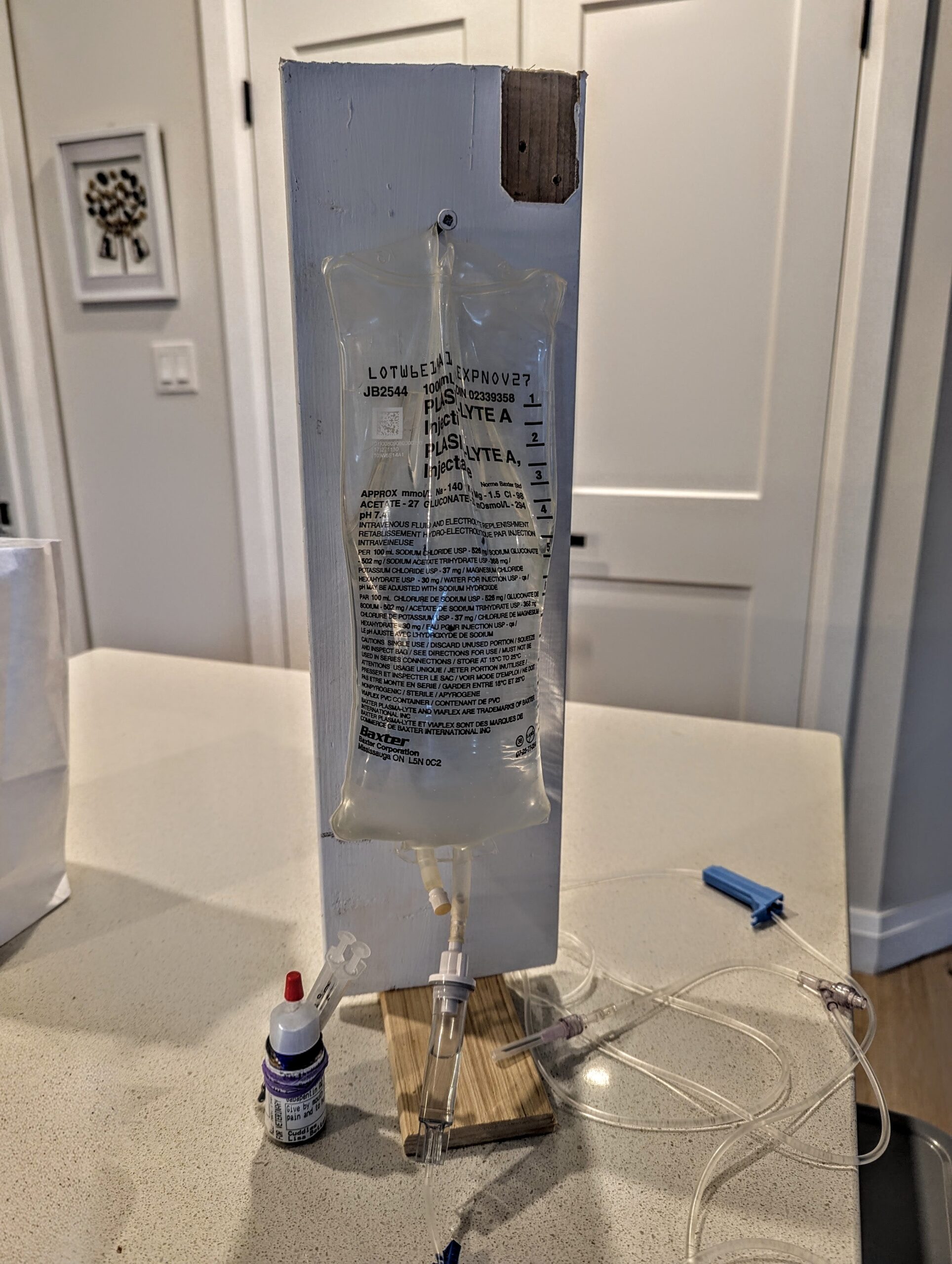 IV bag hanging from a screw wooden stand that Derek made in a hurry. The line and needle are visible.