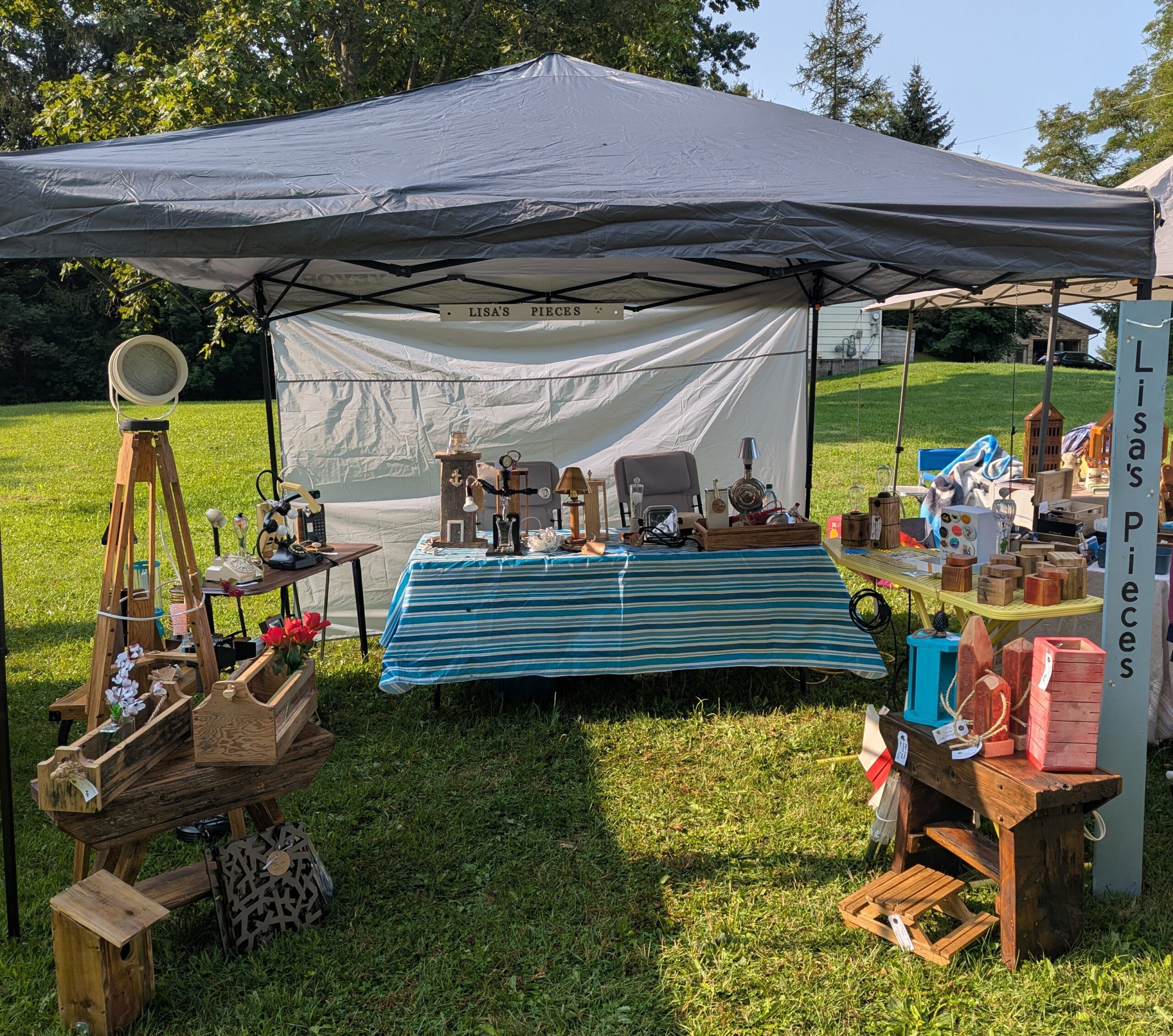 Our booth set up with a grey tent with a back wall, a long table at the back with a blue tablecloth and various tables with merch on them.